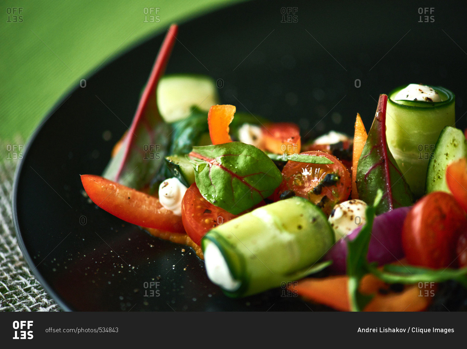 Dish from chef. Extreme close-up shot of delicious vegetable salad with cucumber and cheese rolls, cherry tomatoes, chard leaves served on black plate