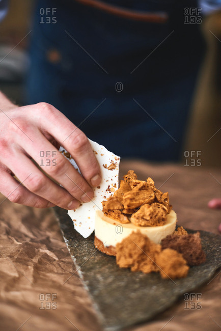 Culinary art. Hand of confectioner decorating small elegant lemon cake with piece of white meringue, close-up view