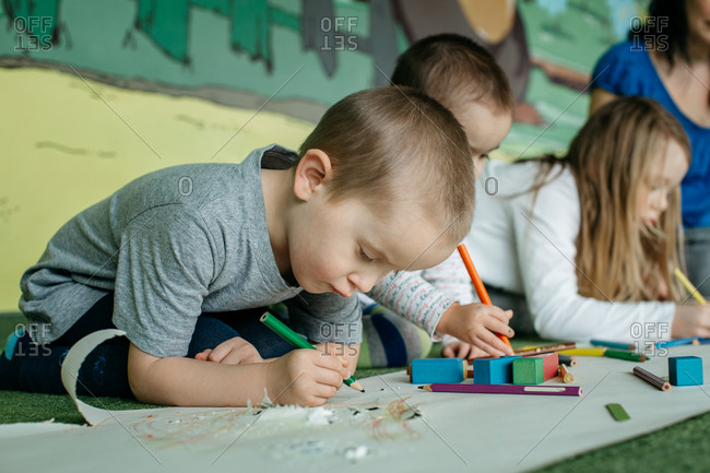 Children sitting on the floor and drawing pictures with colored pencils