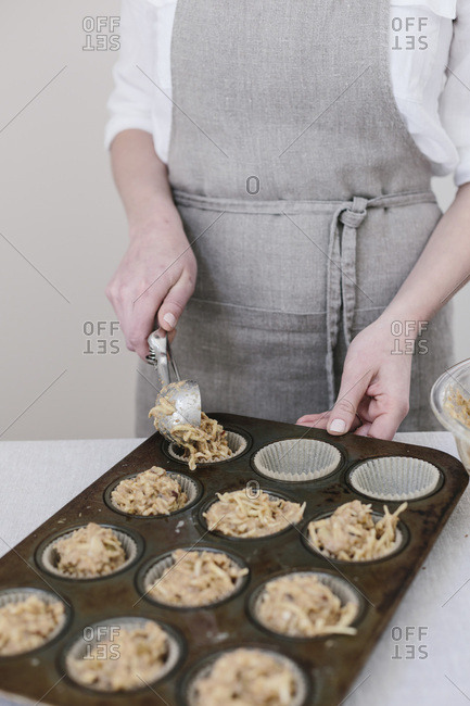 A woman is photographed from the front view as she distributes muffin batter into the muffin tin