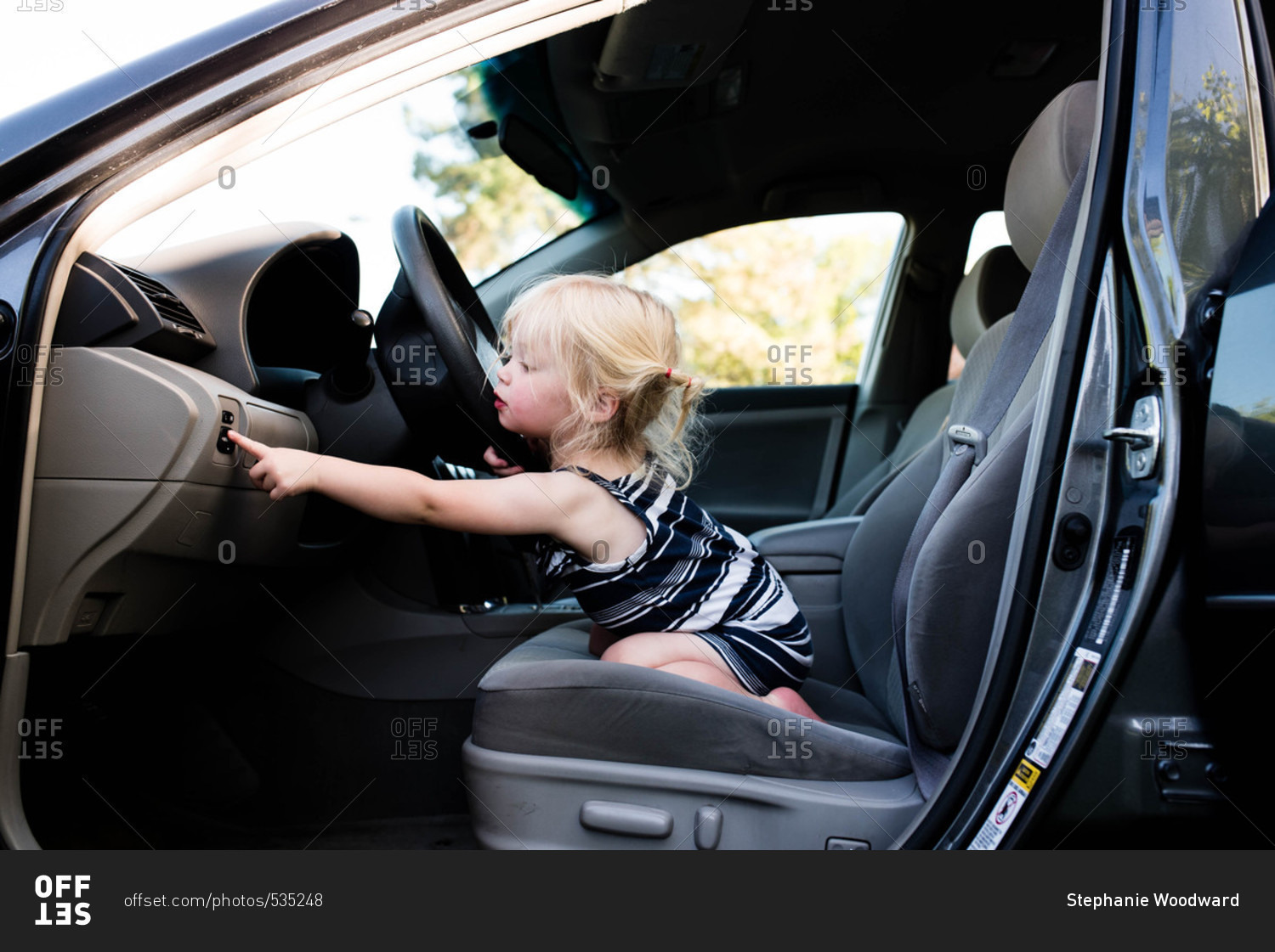 Little girl sitting in front seat of car pressing buttons stock photo