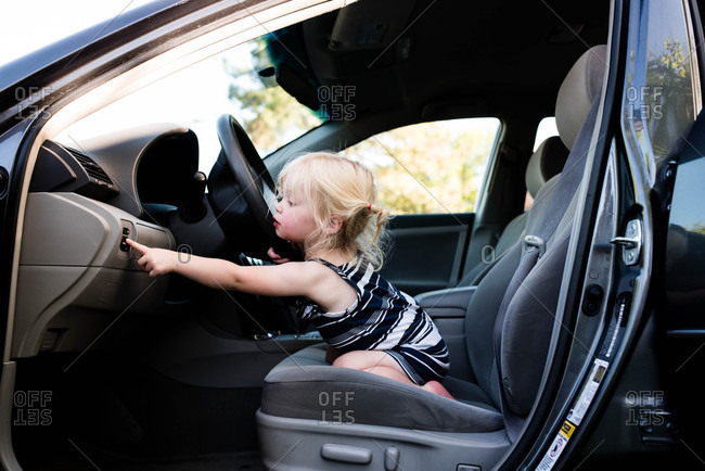 Little girl sitting in front seat of car pressing buttons