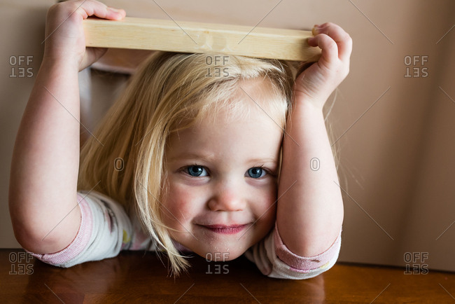 Smiling toddler girl with blonde hair holding wooden block on her head stock photo - OFFSET Smiling toddler girl with blonde hair holding wooden block on her head stock photo - OFFSET