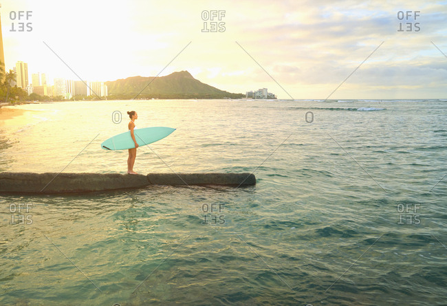 Pacific Islander woman holding surfboard on jetty