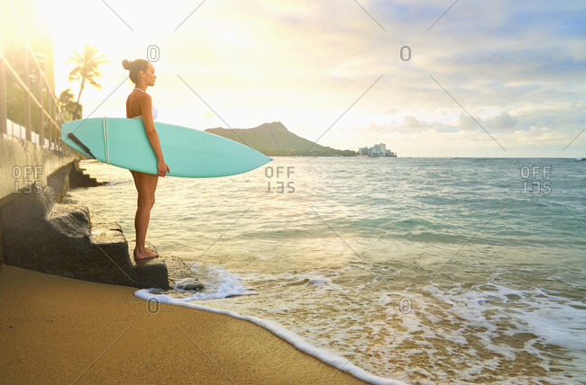 Pacific Islander woman holding surfboard on staircase at ocean