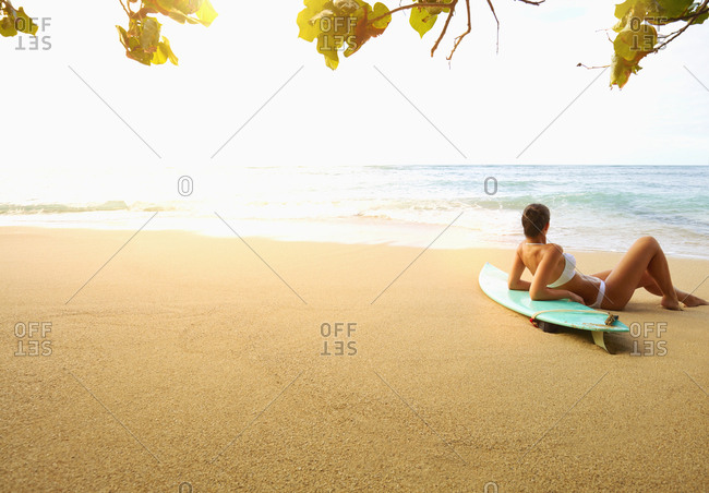 Pacific Islander woman laying on surfboard at beach