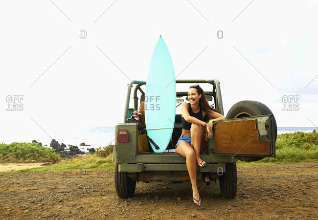 Pacific Islander woman relaxing in off-road vehicle with surfboard