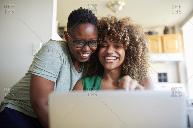 Laughing Black women hugging and using laptop