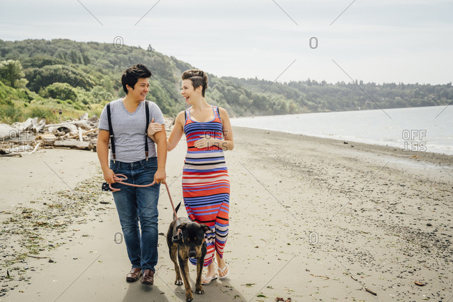 Pregnant lesbian couple walking dog on beach