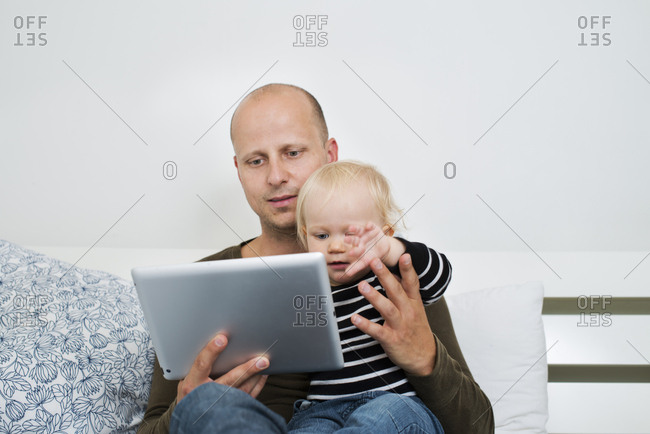 Sweden, Stay at home dad using tablet while holding son
