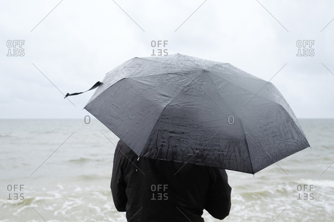 Poland, Niechorze, Woman under black umbrella watching Baltic Sea
