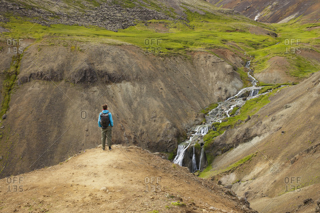 Iceland, Sudurland, Hveragerdi, Reykjadalur, Tourist looking at stream and waterfalls in rocky valley