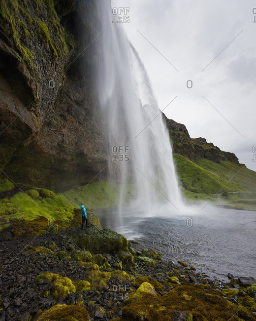 Iceland, Sudurland, Hiker looking up at Seljalandsfoss waterfall