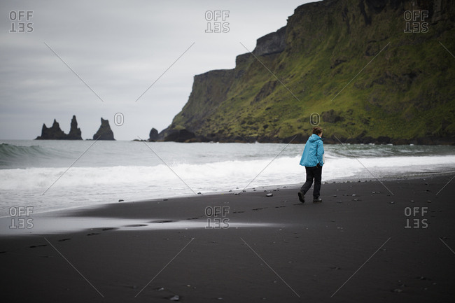 Iceland, Sudurland, Vik i Myrdal, Hiker walking on black sand beach at feet of cliff