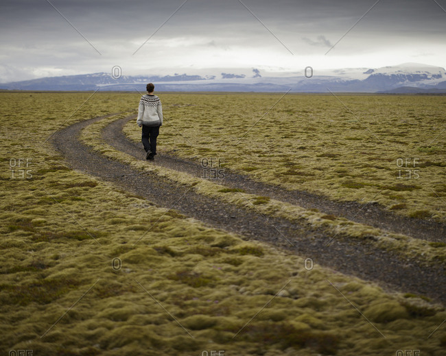 Iceland, Sudurland, Hiker on dirt road through wilderness towards mountain range on horizon