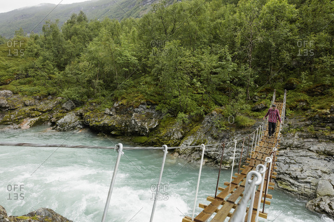 Norway, Jotunheimen, Utladalen, Man walking on suspension bridge over river