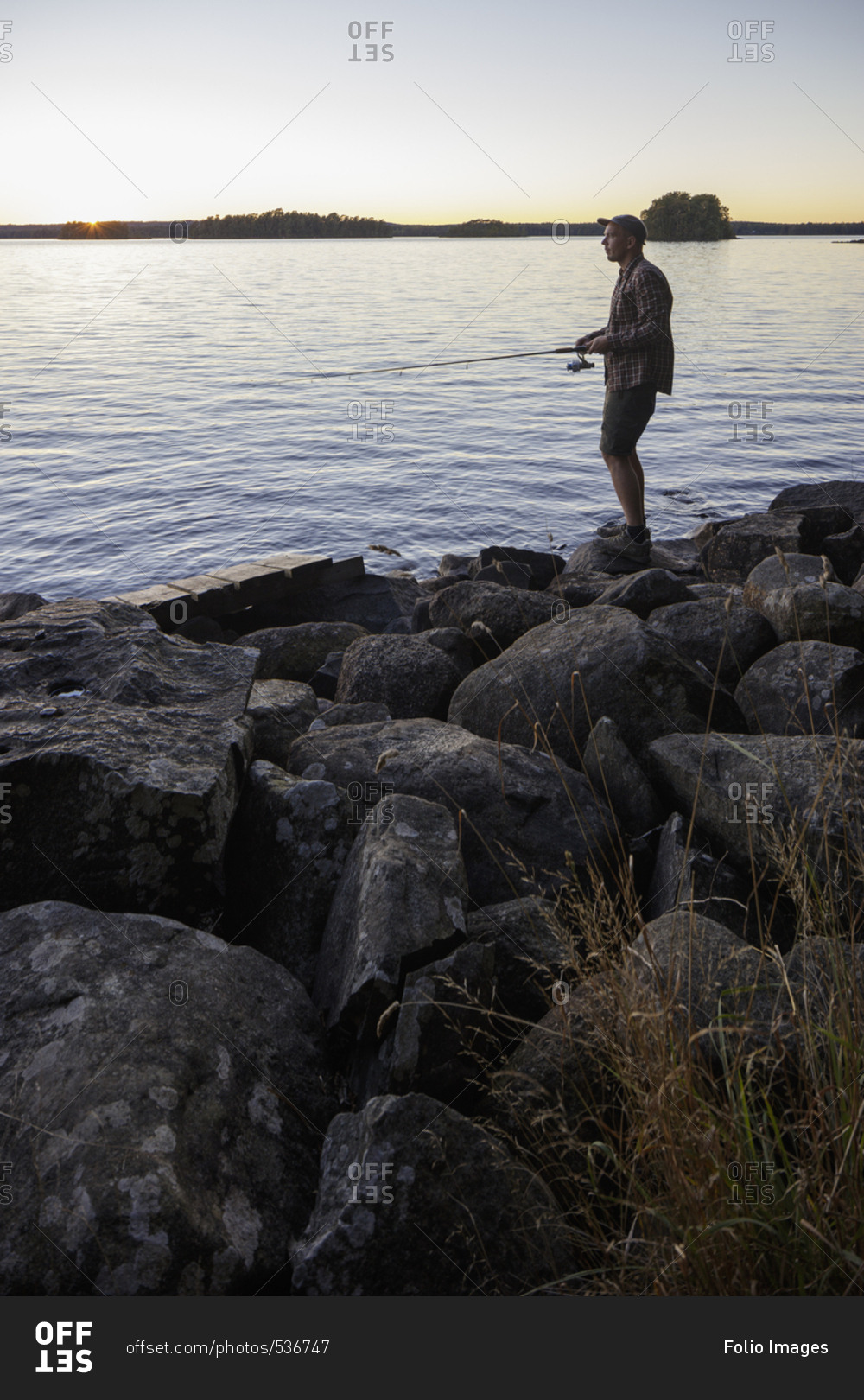 Sweden, Skane, Immeln, Man fishing in lake at sunset