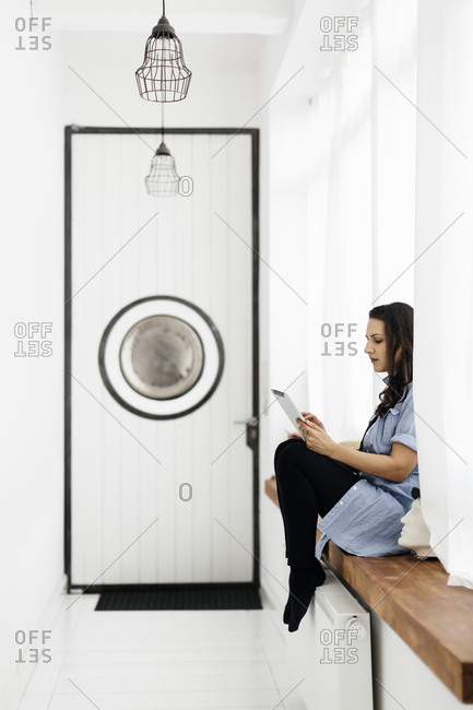 Germany, Woman sitting on window sill and using tablet
