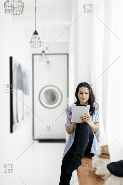 Germany, Woman sitting on window sill and using tablet