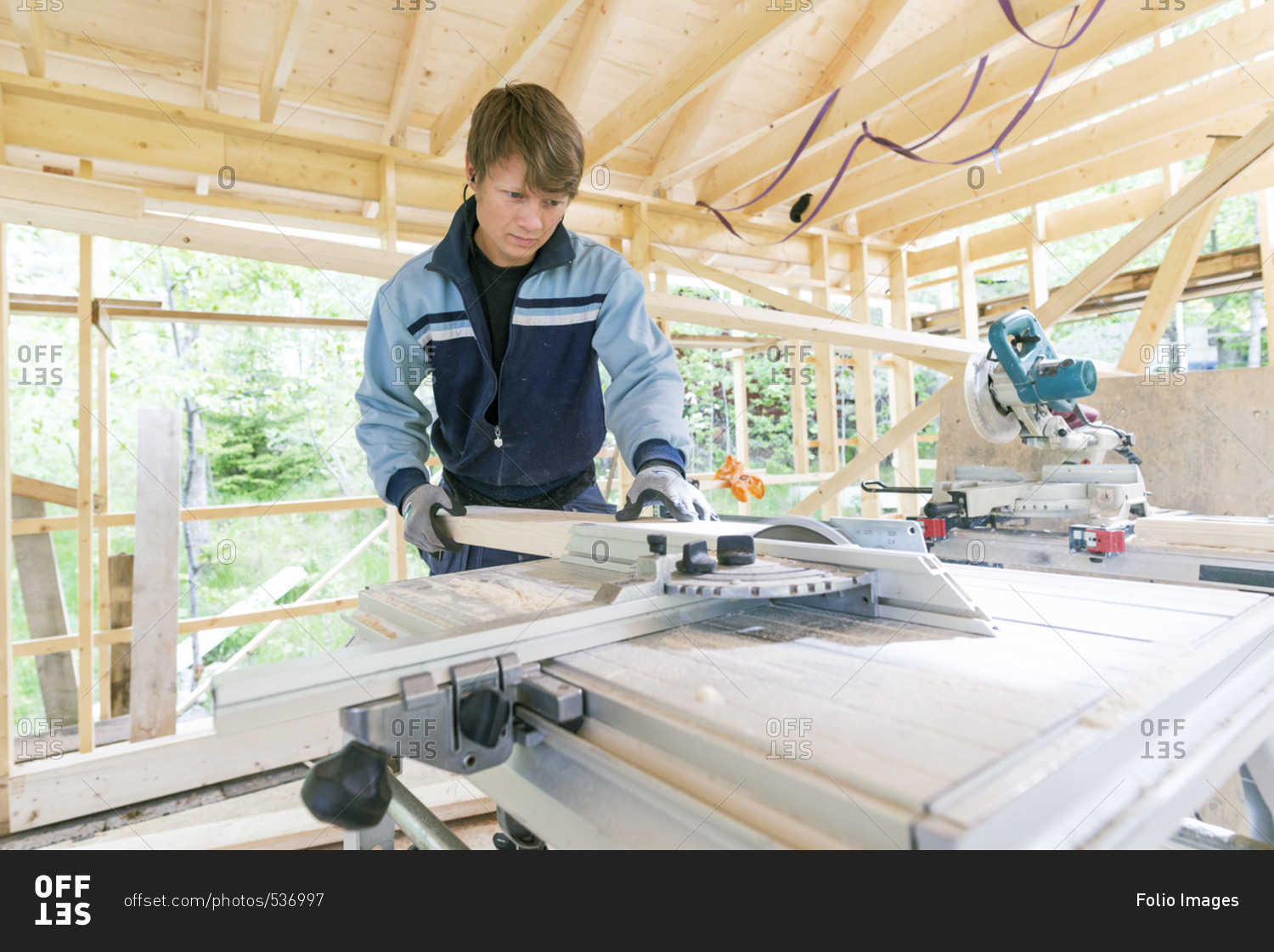 Sweden, Sodermanland, Mid adult man cutting wood with electric saw