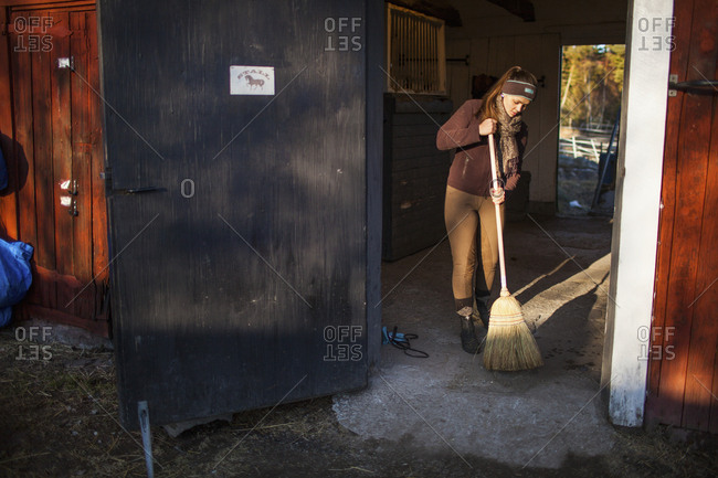 Sweden, Uppland, Faringso, Woman sweeping in barn