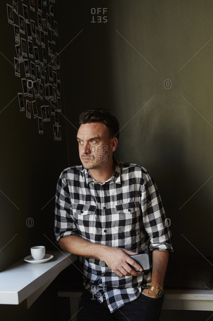 Sweden, Pensive man in cafe looking away and holding mobile phone