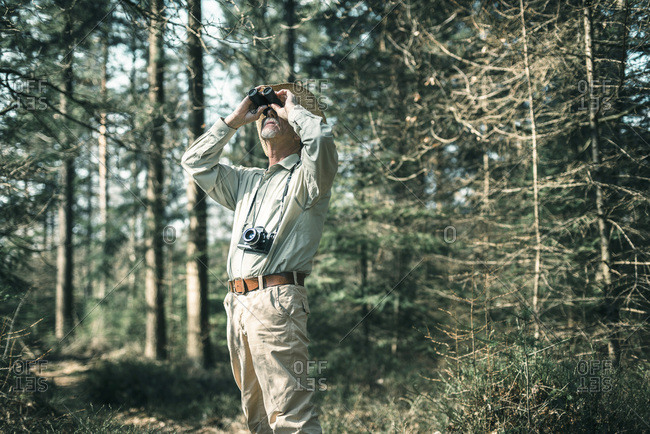 Man looking with binocular in forest.