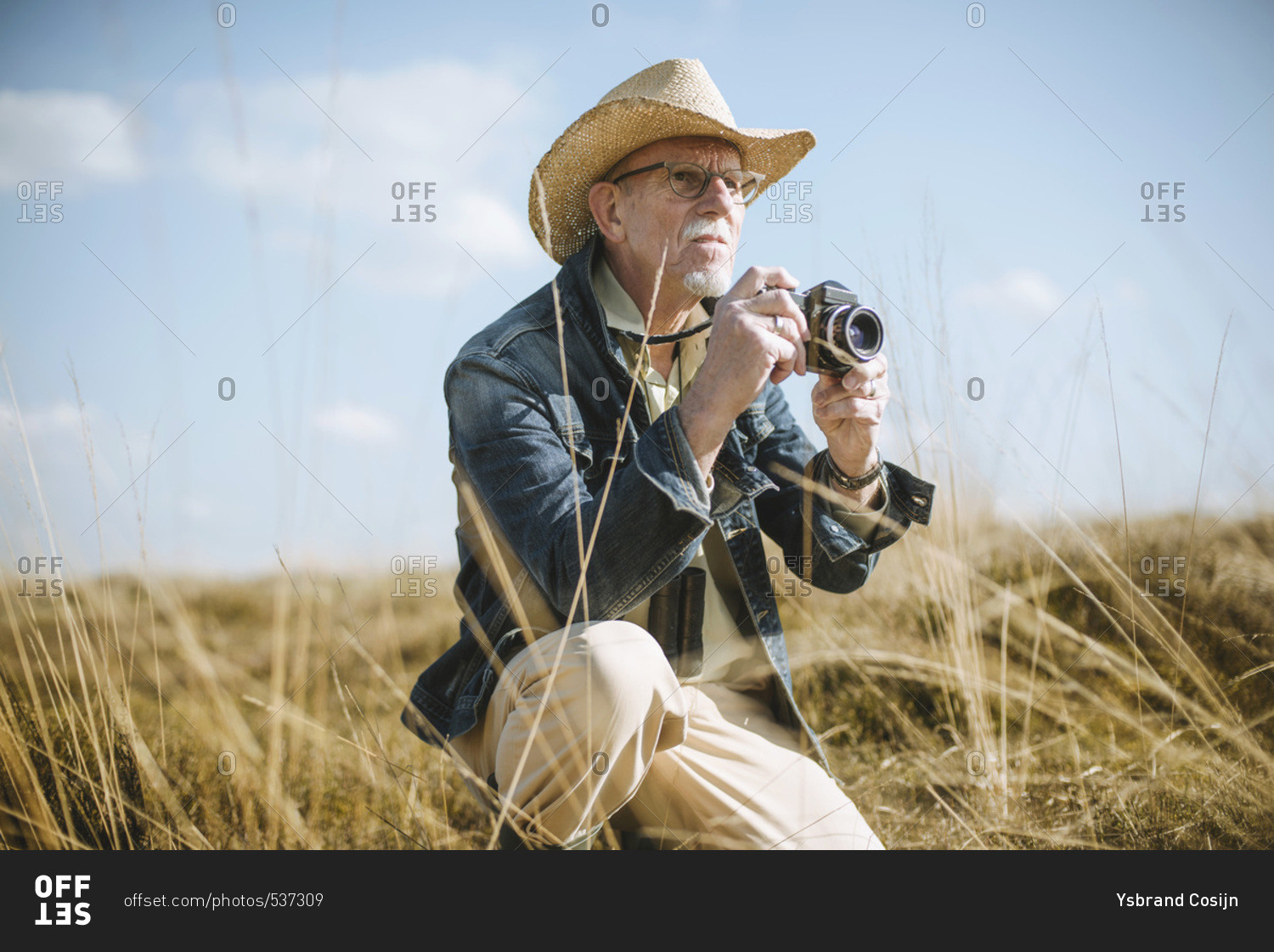 Safari man sitting with camera in field.