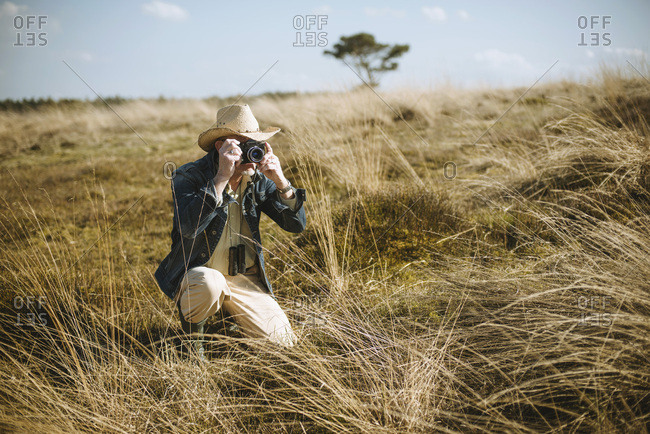 Safari man sitting with camera in field.