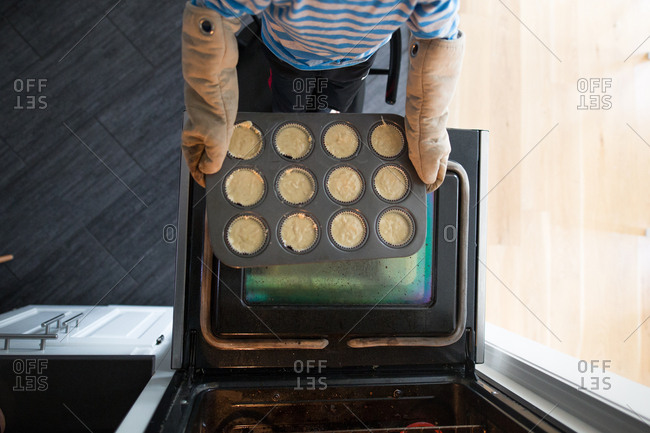Boy wearing oven mitts putting muffin tin into oven