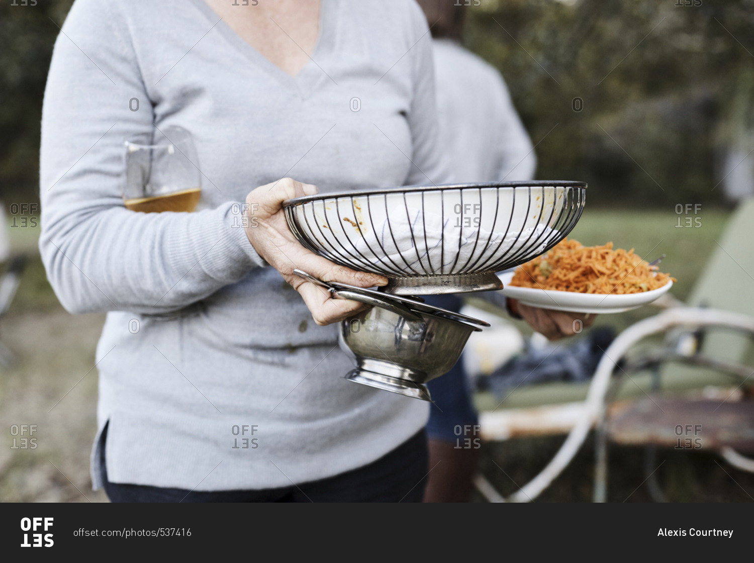Woman with hands full carrying serving dishes at outdoor dinner