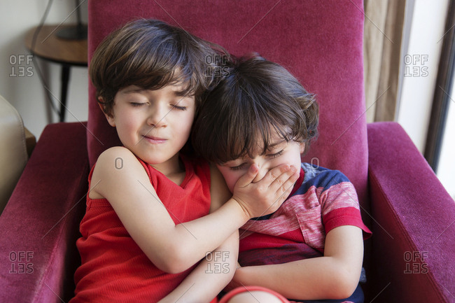Twin brothers sitting together on arm chair keeping silence