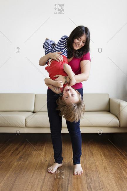 Smiling mother holding her little son upside down in the living room