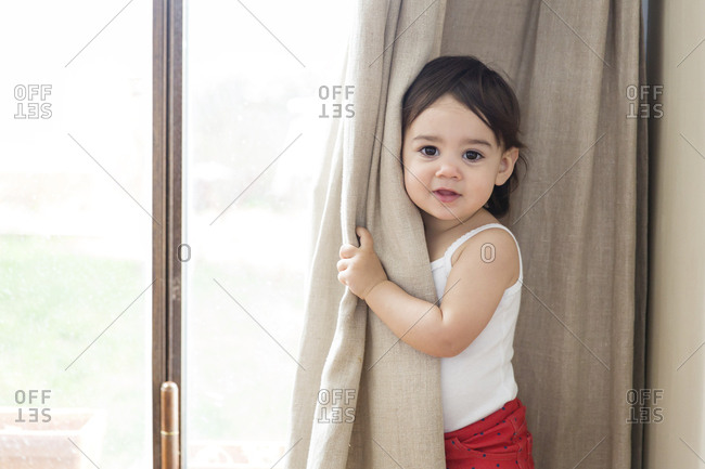 Portrait of a toddler girl playing peek-a-boo behind the curtain