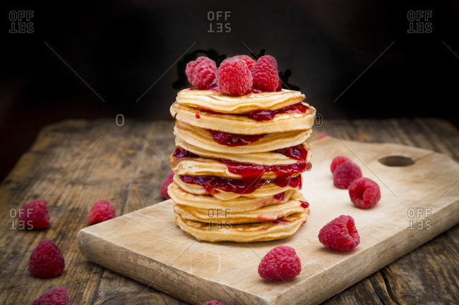 Stack of pancakes with raspberries and raspberry jam on wooden board