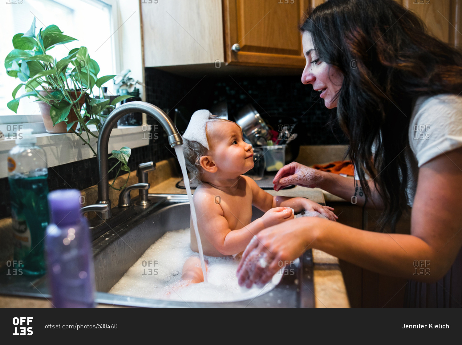 Mom giving baby a bubble bath in kitchen sink