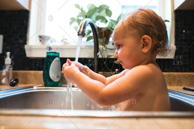 Baby Playing With Water While Getting A Bath In The Kitchen