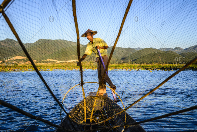 Asian fisherman using fishing net in canoes on river