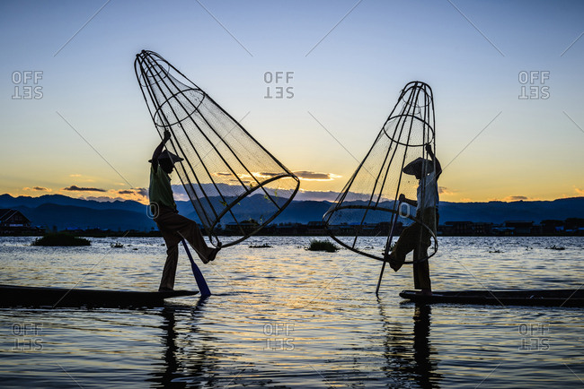 Asian fishermen using fishing nets in canoe on river