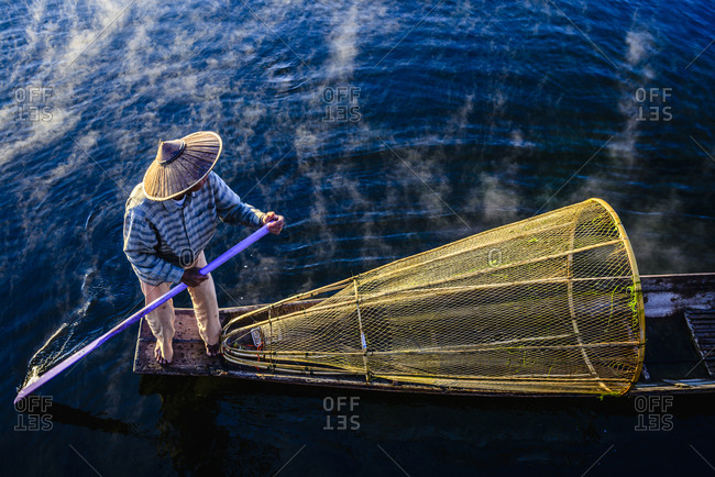 High angle view of Asian fisherman using fishing net in canoe on river