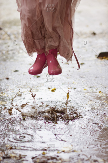 Caucasian girl in rain boots jumping in rain puddles