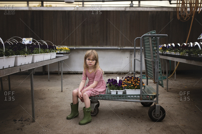 Young girl in glasses sitting on cart in garden center