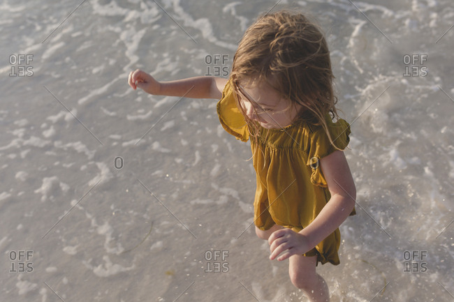 Young girl in yellow dress playing in the ocean surf