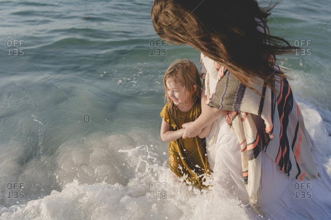 Mother and daughter smiling as waves crash around them in the ocean and the sun shines on their faces