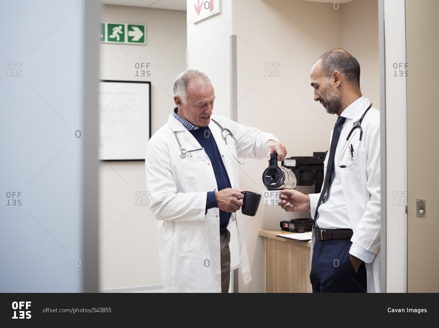 Doctors having coffee while standing in hospital seen through door