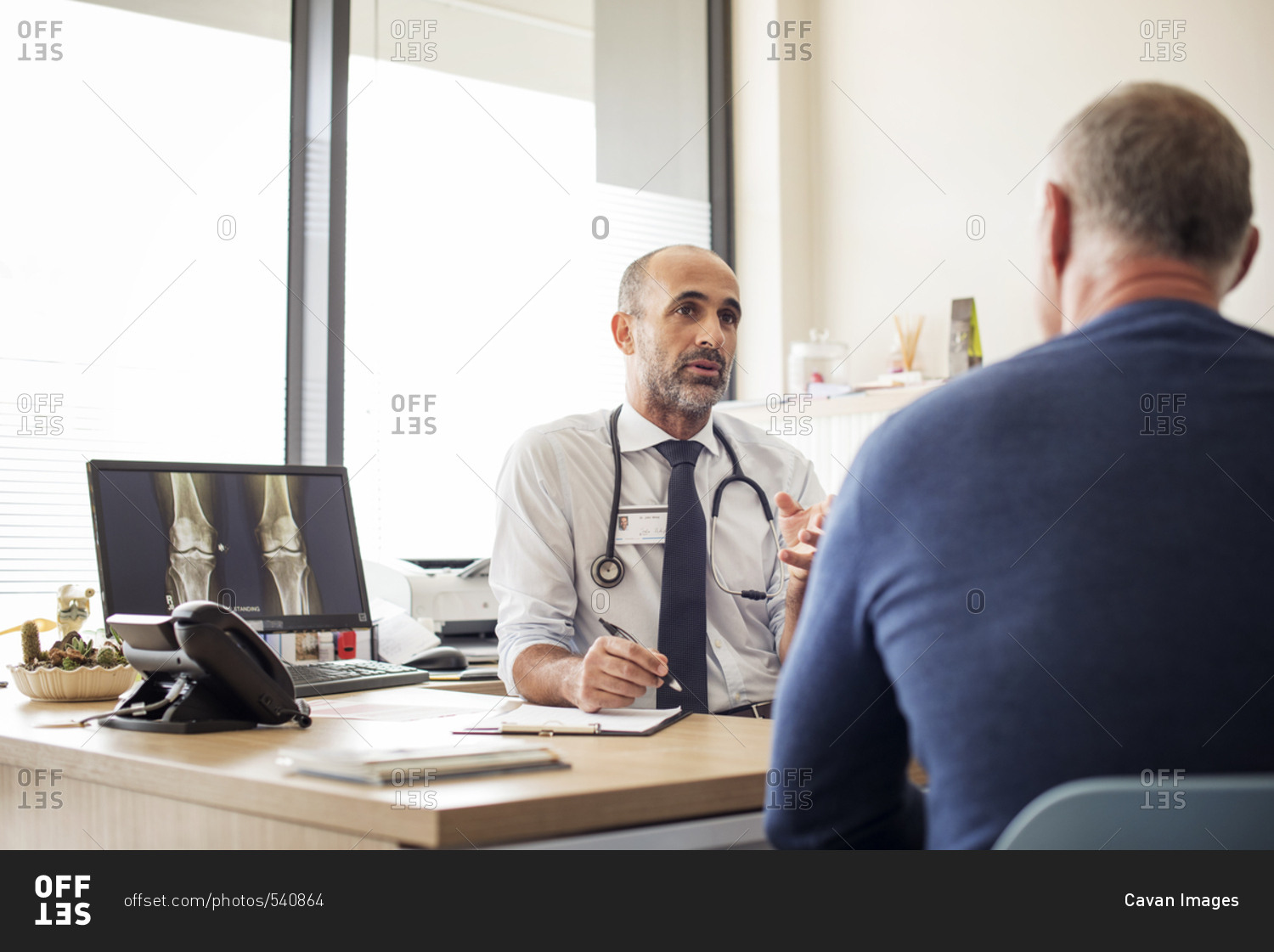 Doctor discussing with patient while sitting at desk in hospital