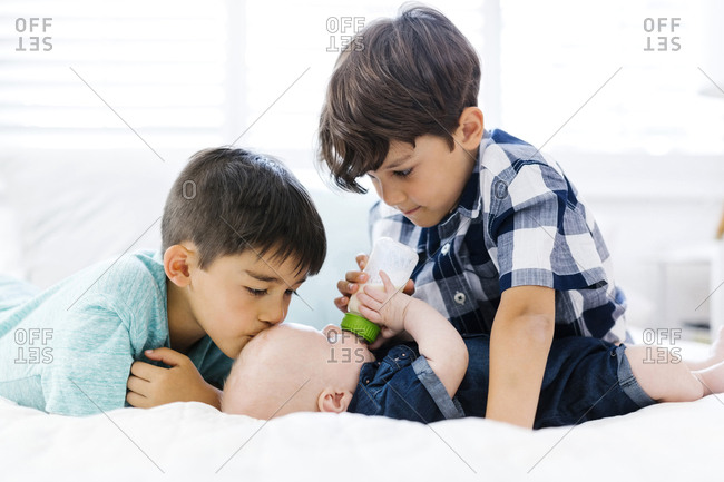 Older brothers feeding small brother lying on bed