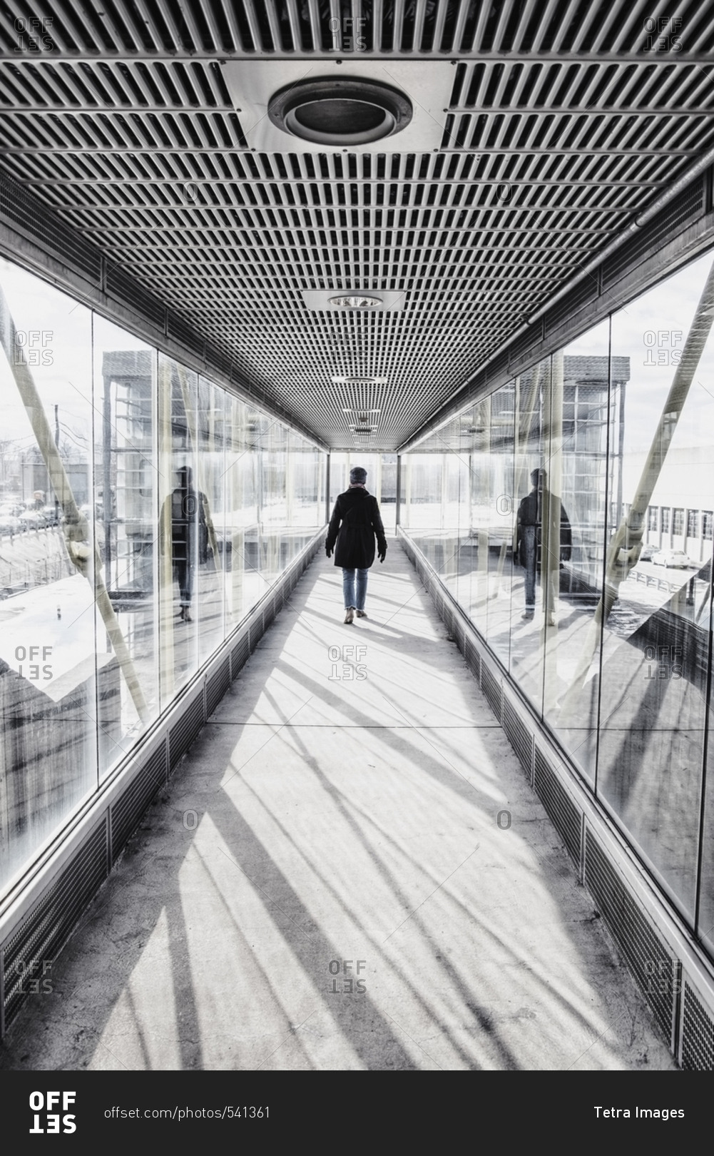 USA, Massachusetts, Boston, Woman walking down glass and metallic walkway at train station