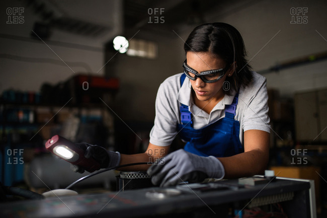 female mechanic looking for a fault on a compressor engine using a flashlight