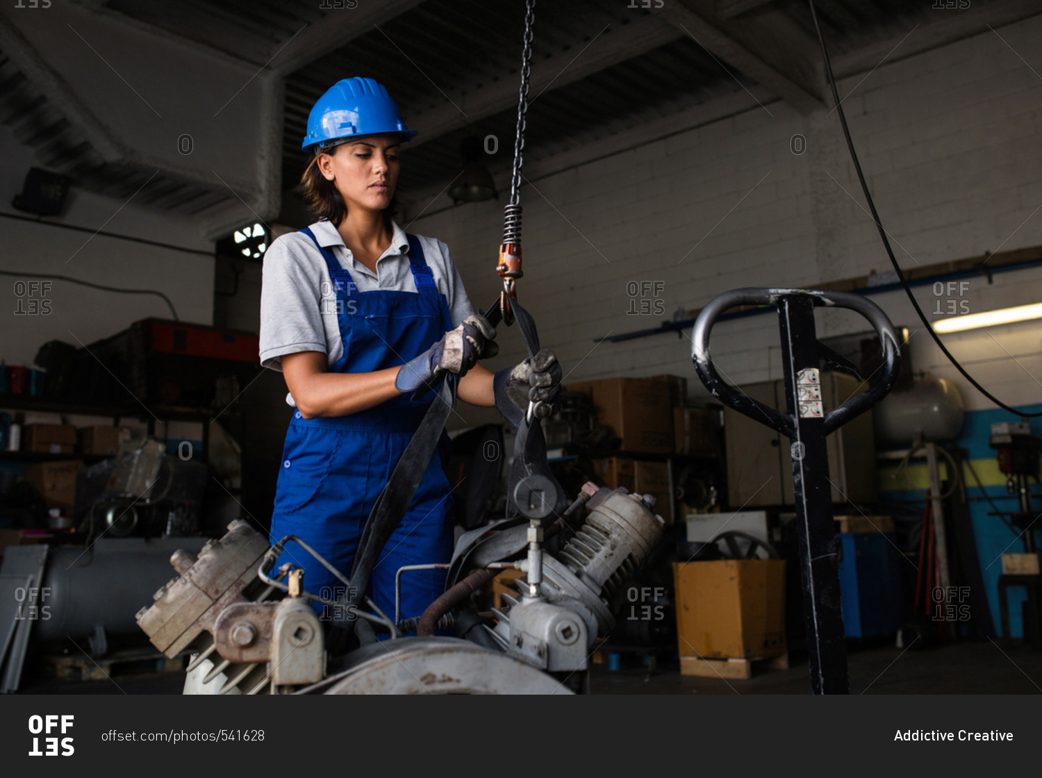 Female mechanic operating a hoist to lift a compressor engine